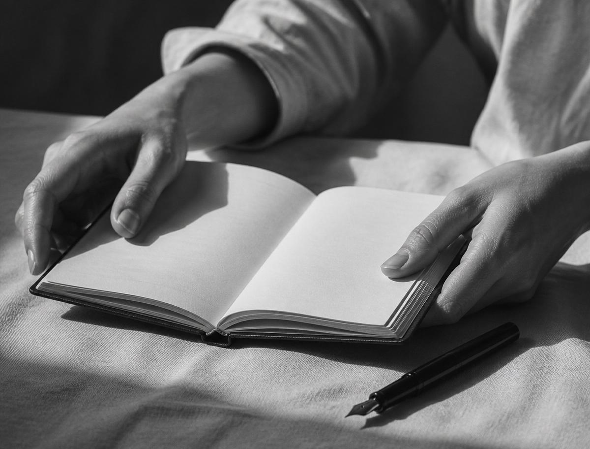 Monochrome close-up of hands beside an open notebook